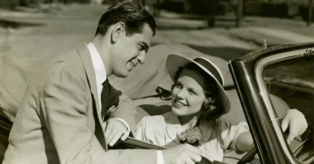 Man leaning against car chatting with woman in driver's seat